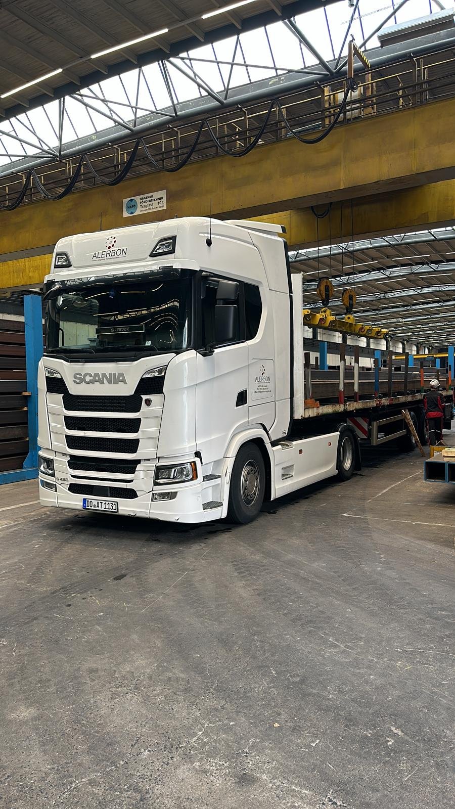 Weißer ALERBON Scania S450 beim Beladen mit Stahlträgern in einer Halle